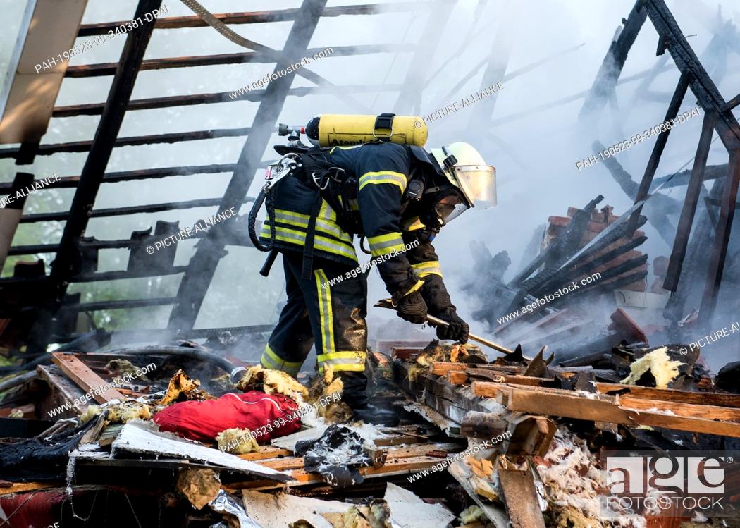 Stock Photo: 23 May 2019, Schleswig-Holstein, Wohltorf: A firefighter pulls apart debris from a house that was destroyed in a fire. The fire department was still looking for.