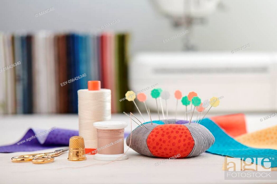 Stock Photo: Pin cushion, brightly colored strips of fabric, sewing accessories on the background of stack of fabrics and sewing machine.
