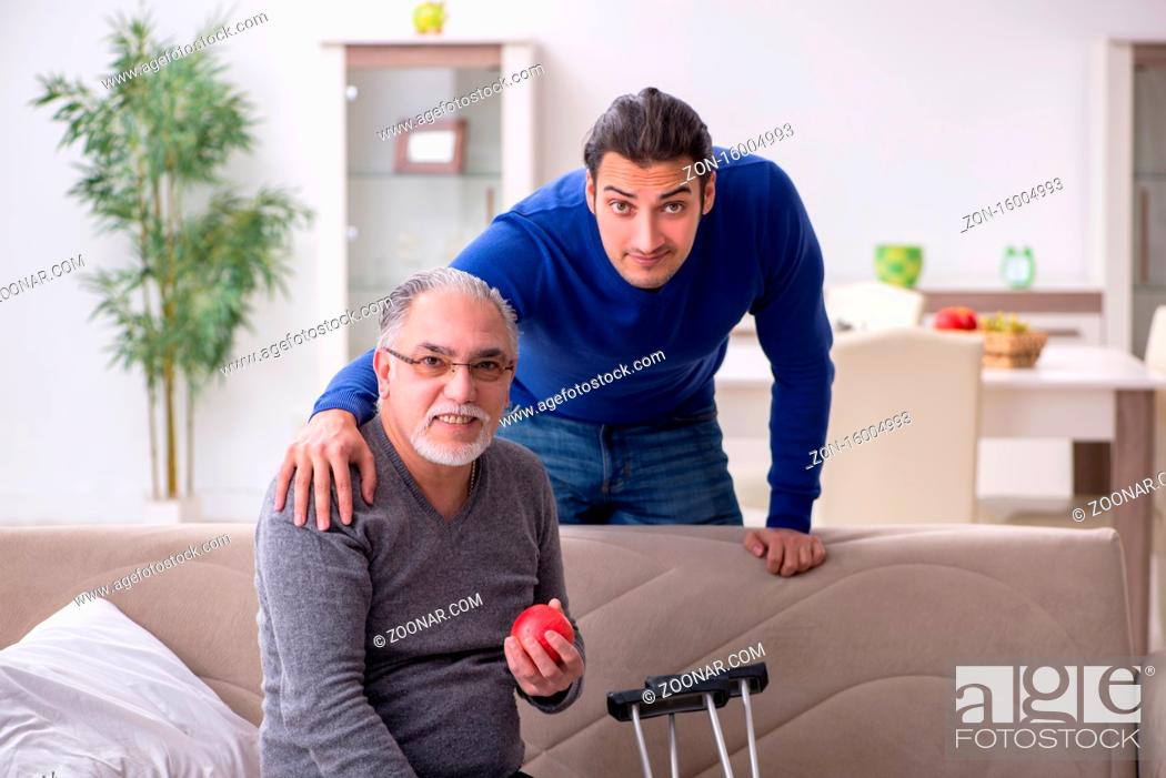 Stock Photo: Young man looking after his leg injured dad.