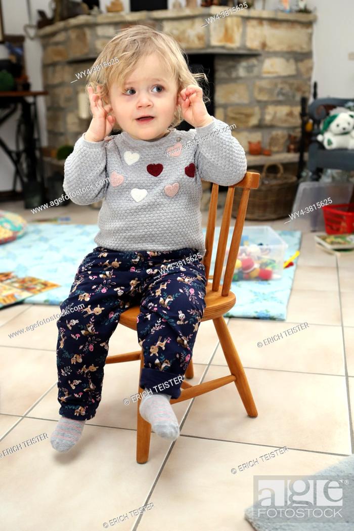 Stock Photo: little girl sitting on a wooden child chair in living room and covers her ears.