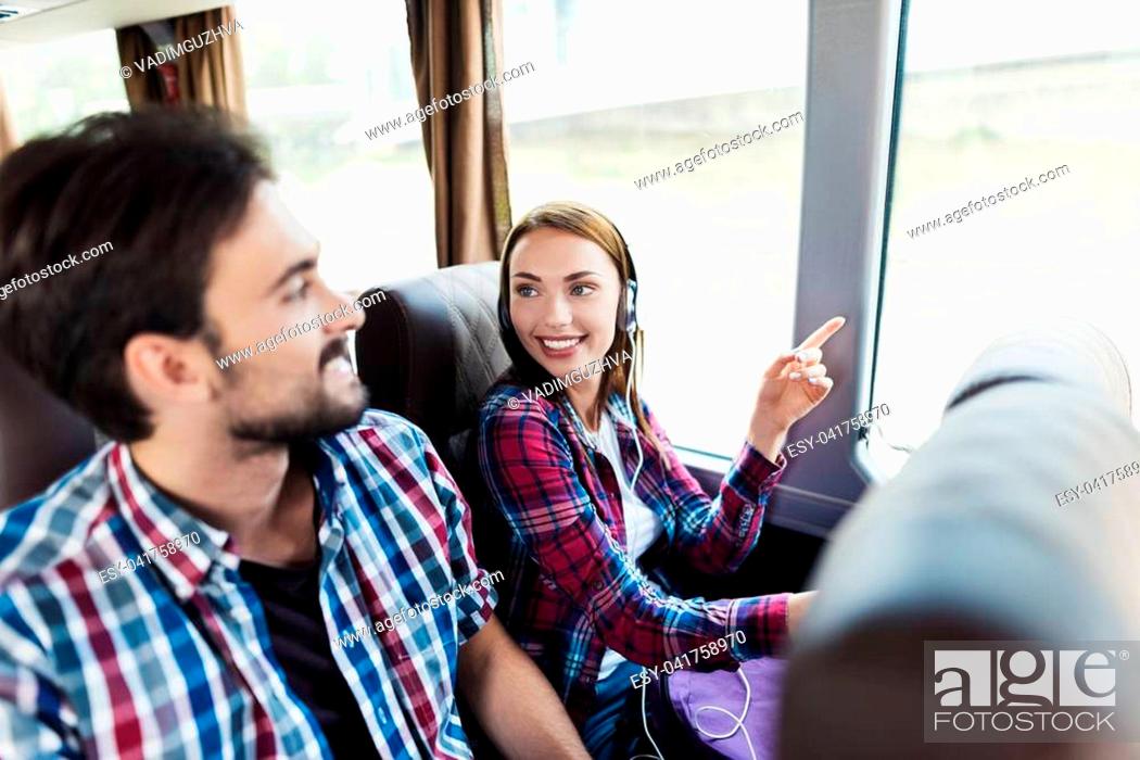 Imagen: The guy and the girl are on the bus. The girl has headphones. He and the guy are discussing something and smiling. Behind them sit other tourists who are.
