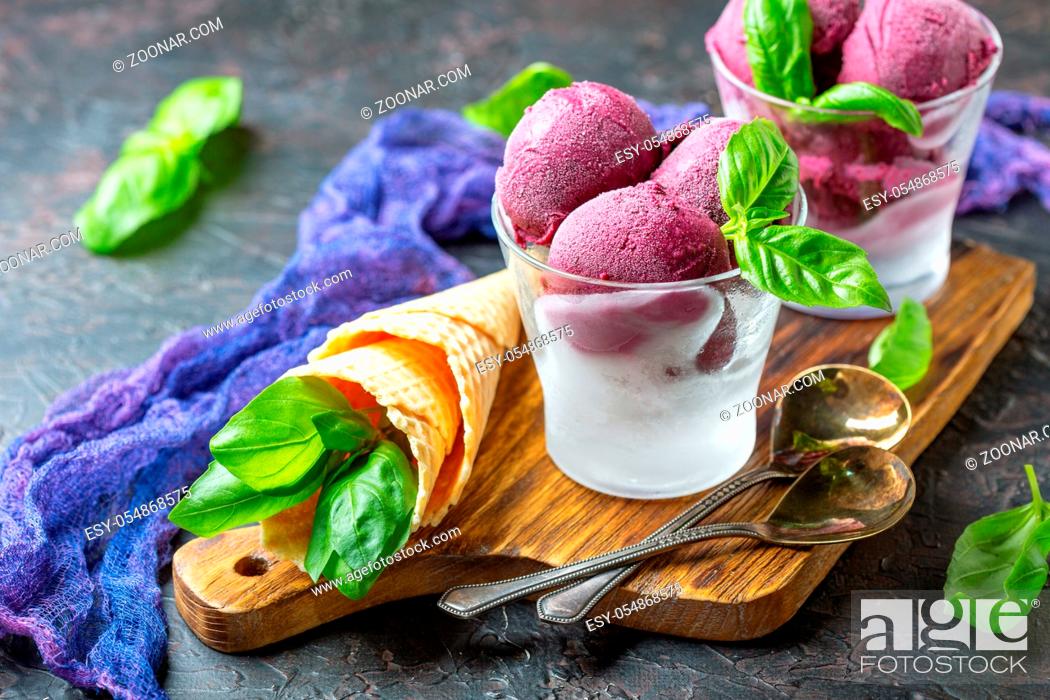 Stock Photo: Artisanal blueberry ice cream in glasses with green basil on a wooden serving board on a dark textured background. Selective focus.