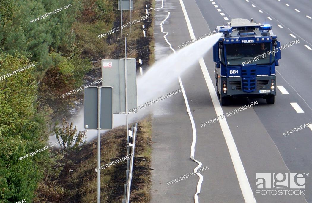 Stock Photo: 27 July 2018, Germany, Potsdam/Fichtenwalde: A police water cannon extinguishes on the edge of a forest area on the motorway.