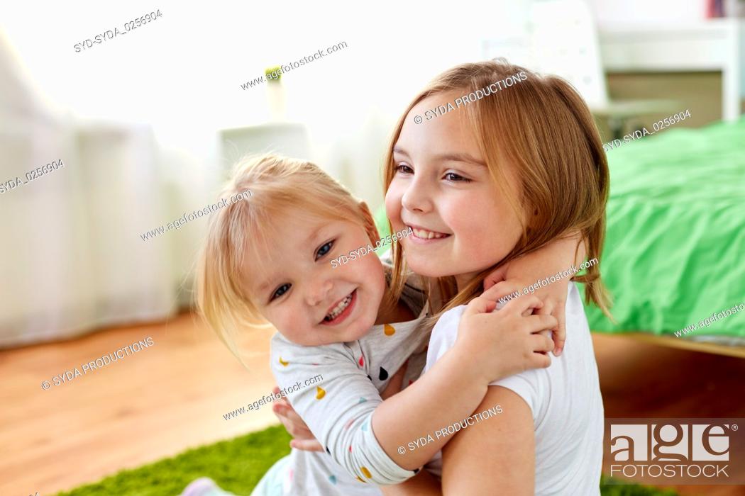 Stock Photo: happy little girls or sisters hugging at home.