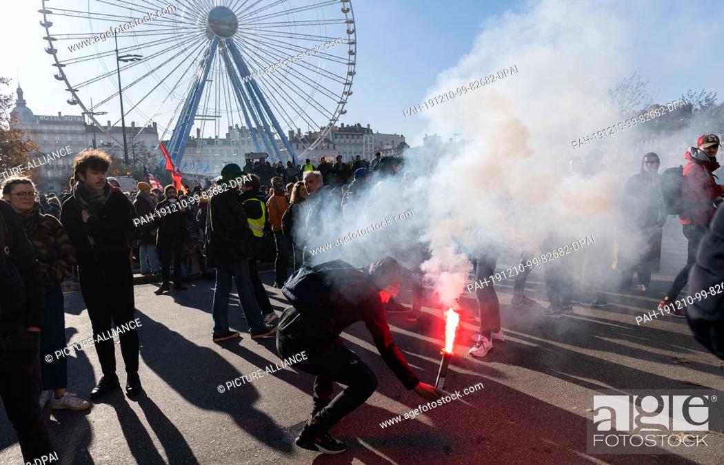 Stock Photo: 10 December 2019, France (France), Lyon: A demonstrator ignites pyrotechnics during a demonstration in the context of strikes and protests against the pension.
