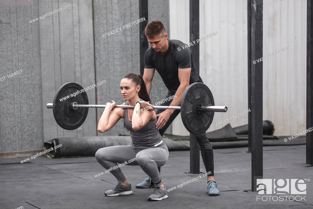 Stock Photo: Male instructor assisting young woman crossfit training at gym.