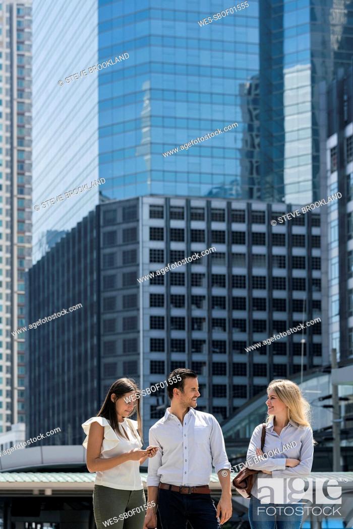 Photo de stock: Smiling business colleagues talking in the city in front of skyscraper.