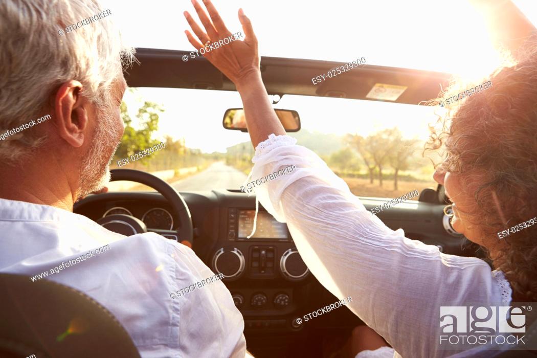 Stock Photo: Mature Couple Driving Along Country Road In Open Top Car.