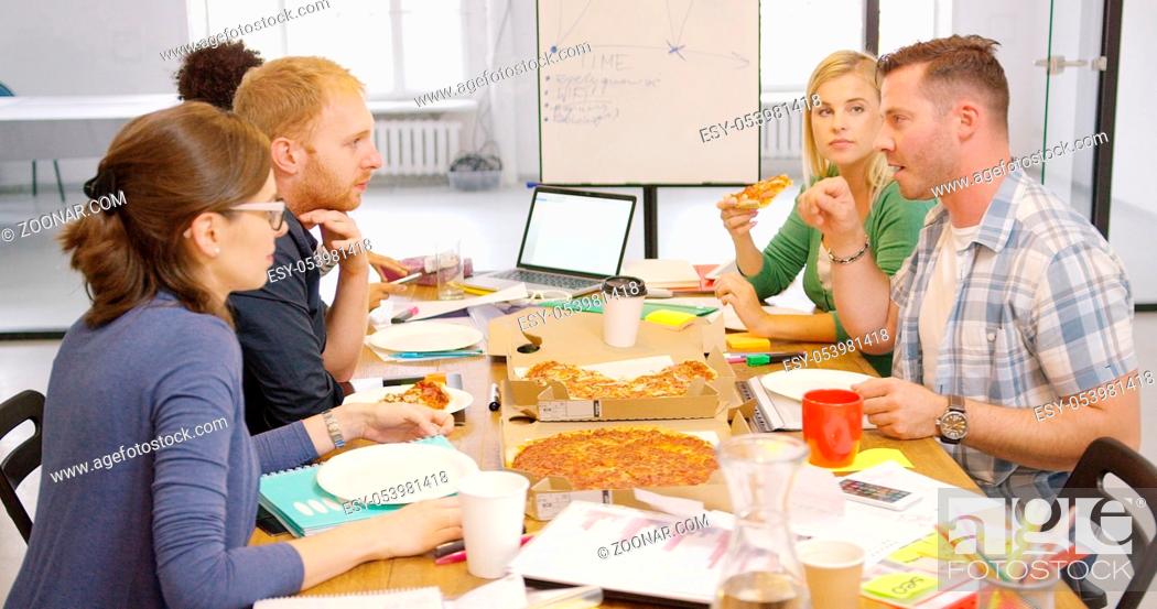 Stock Photo: Side view of friendly colleagues relaxing at table in office having ordered pizza and talking lively while resting.