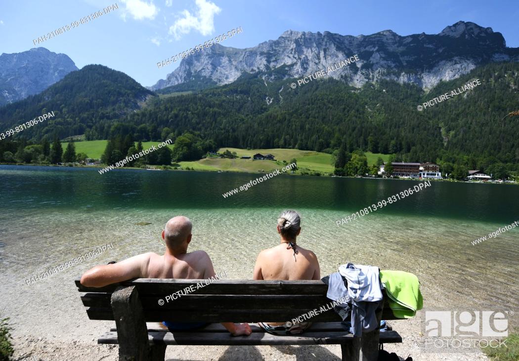 Stock Photo: 13 August 2021, Bavaria, Hintersee: A couple enjoys the cool Hintersee with their feet in the water. The mountain lake lies at over 789 above sea level.