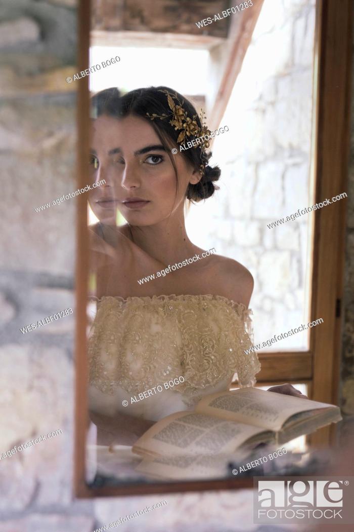 Stock Photo: Young woman in wedding dress with book looking at mirror.