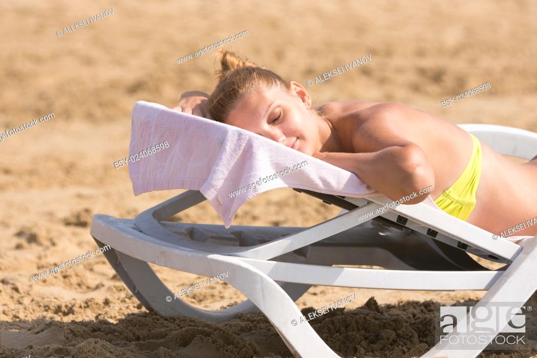 Stock Photo: Young girl is lying on a deck chair on his stomach, his head turned and eyes closed.