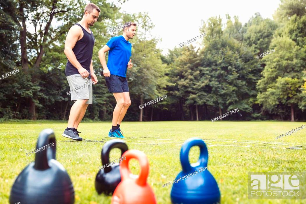 Stock Photo: Colorful kettle bells in front of two athletic men training on agility ladder at park.