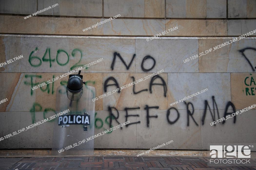 Stock Photo: A ESMAD riot shield and helmet are layed over a wall that reads ""No to the tax reform"" as citizens and demonstrators support the congress sesion in which.