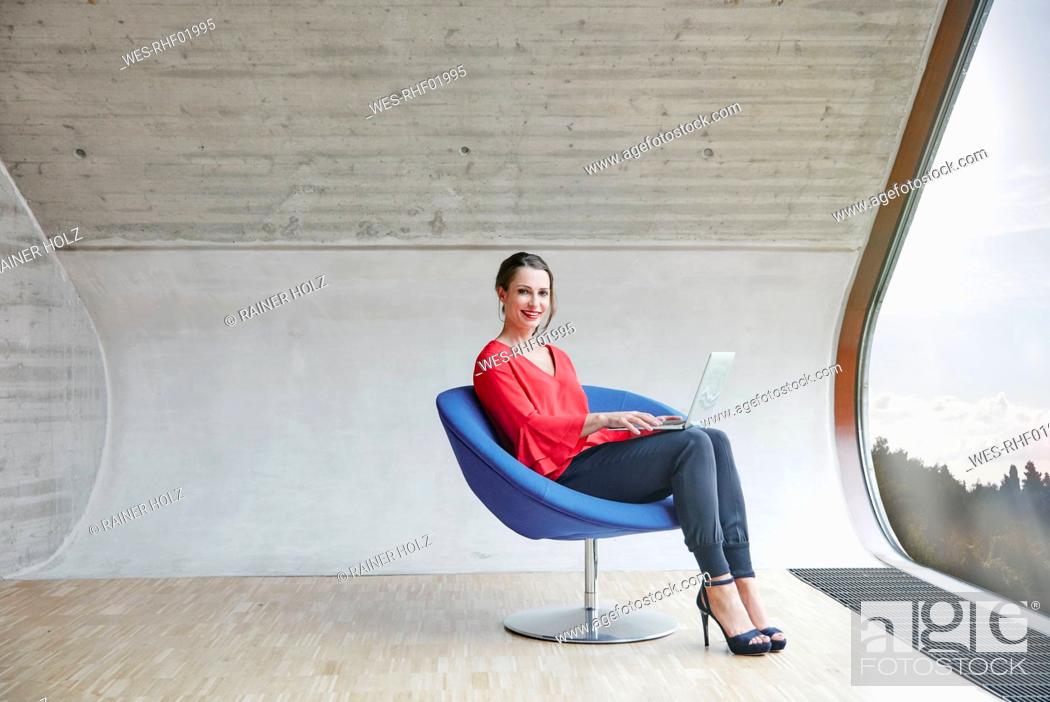 Stock Photo: Portrait of smiling woman sitting on chair in attic office with laptop.