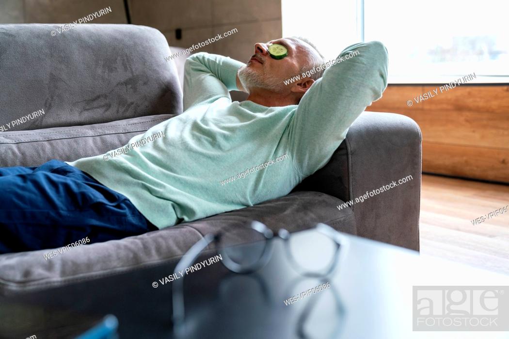 Stock Photo: Man with cucumber slices on eyes lying on sofa at home.