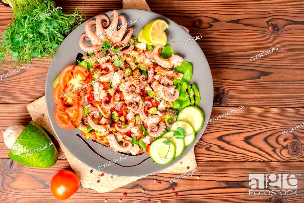 Stock Photo: top view of salad with tentacles of octopus, lime, avocado and lettuce, decorated lime, cucumber, tomato, sprigs of pea leaves and dry peppers, natural seafood.