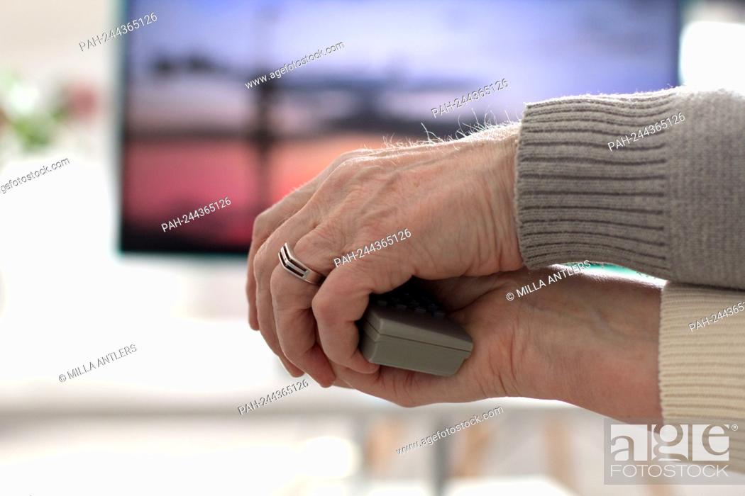 Stock Photo: Elderly couple holding remote together with their hands while watching movie. Old man helping his wife switching channels with TV remote.