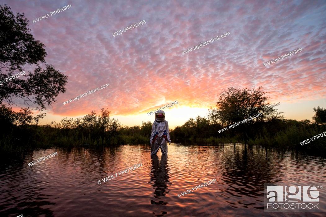 Stock Photo: Spacewoman standing in water at sunset.