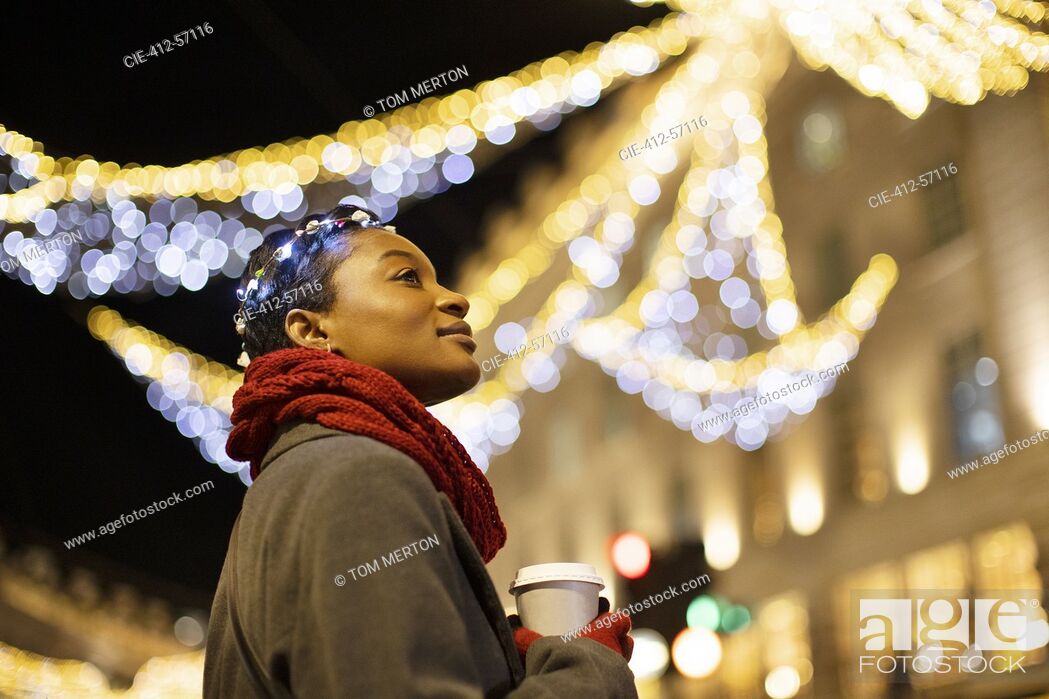 Stock Photo: Serene young woman with coffee in city with lights at night.