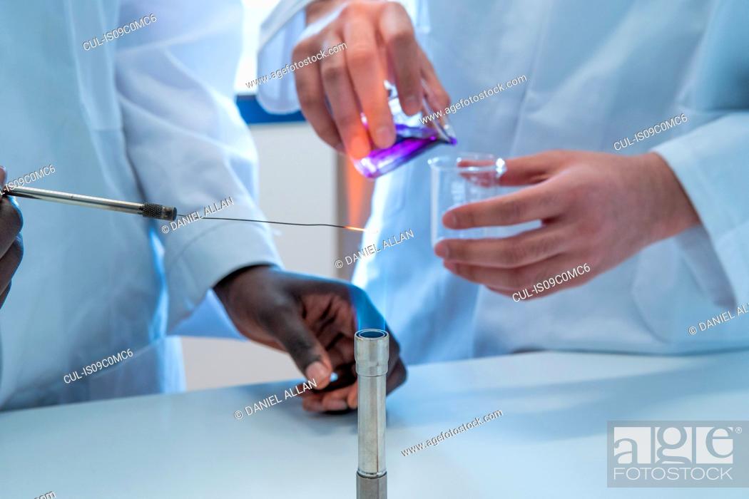 Stock Photo: Young female and male scientists experimenting with liquid and bunsen burner in laboratory, cropped.