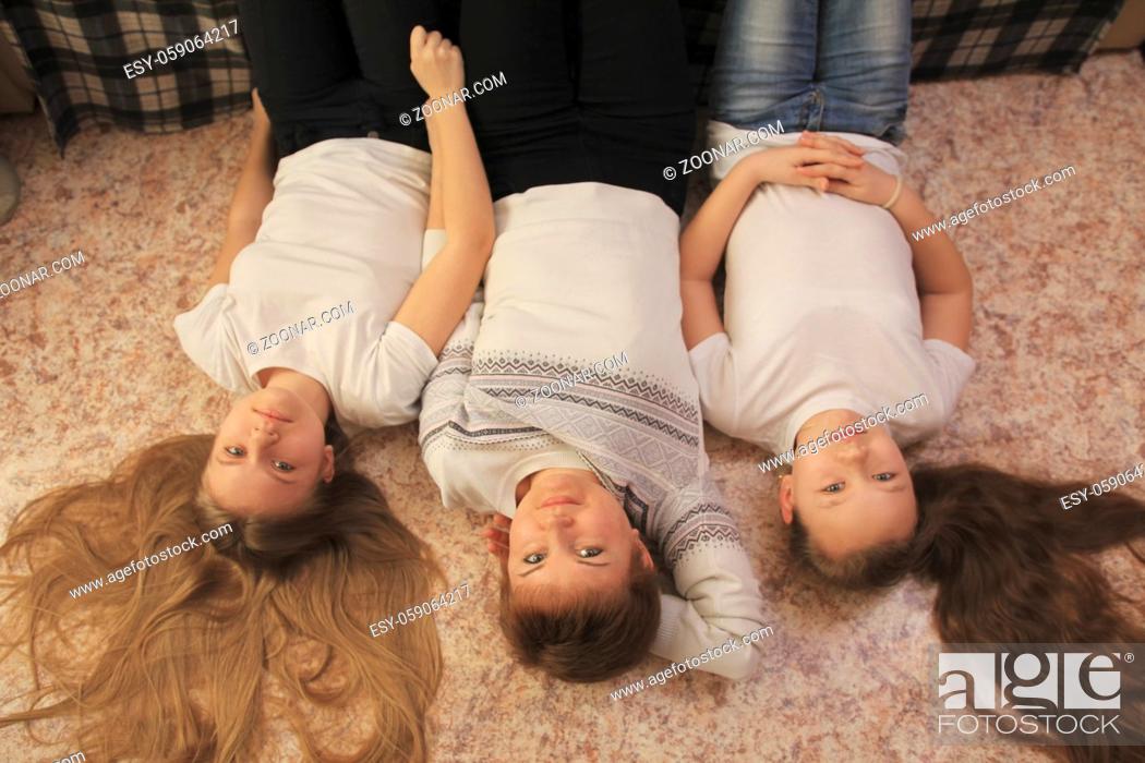 Stock Photo: Young mom and her two teen daughters lying on the floor at home, concept of family relations.