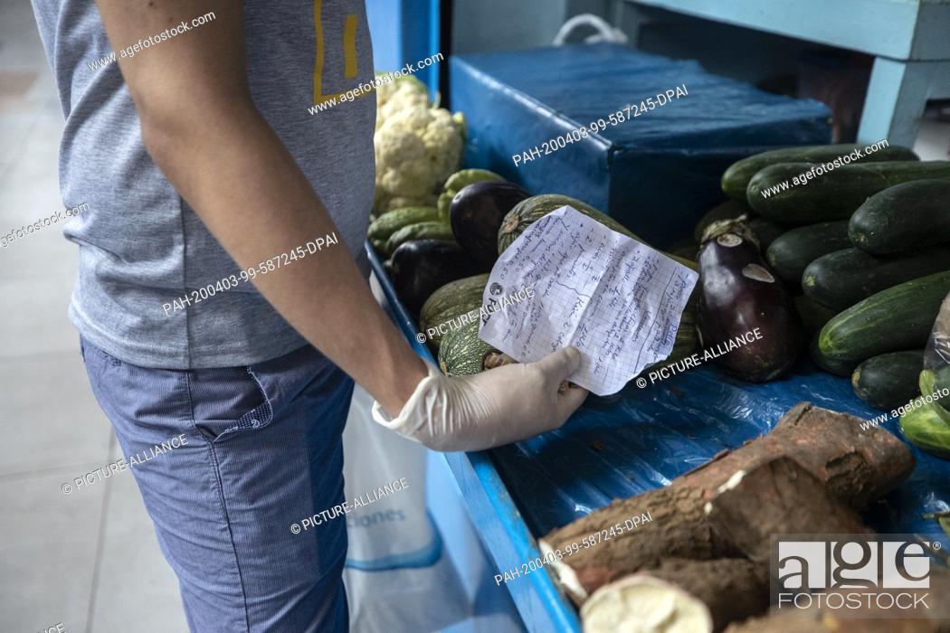 Stock Photo: 03 April 2020, Peru, Lima: A man wearing latex gloves against the spread of the coronavirus holds a shopping list at a vegetable stand in a market.
