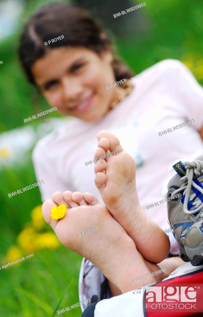 Stock Photo: young darkhaired girl lying in the grass with a flower between her toes.
