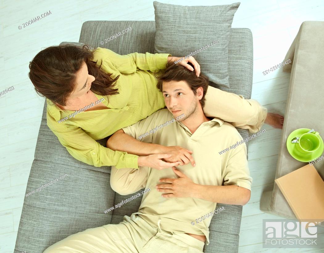 Stock Photo: Young couple resting together on couch at home, embracing. Hing angle shot.