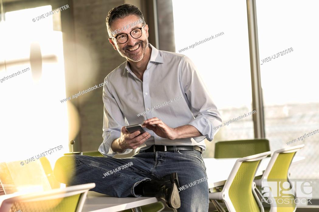 Photo de stock: Happy mature businessman with cell phone in office.