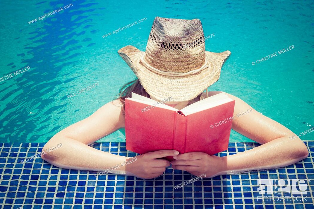 Stock Photo: Woman wearing straw hat reading book at pool edge.