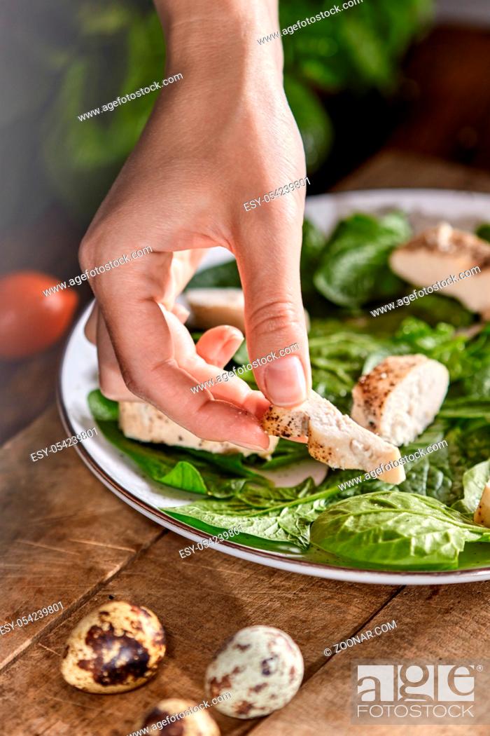 Stock Photo: A plate with spinach on a wooden table. Woman's hand puts a piece of meat in the plate. Step by step cooking healthy dietary salad.