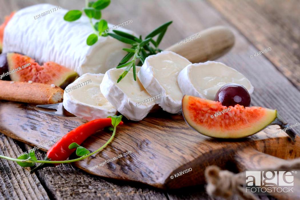 Stock Photo: Goat cheese with figs and black olives on a wooden cutting board.