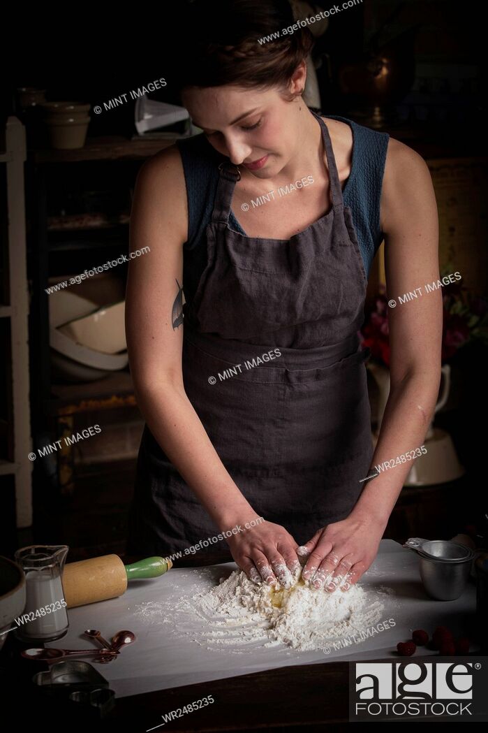 Stock Photo: Valentine's Day baking, young woman standing in a kitchen, preparing dough for biscuits.