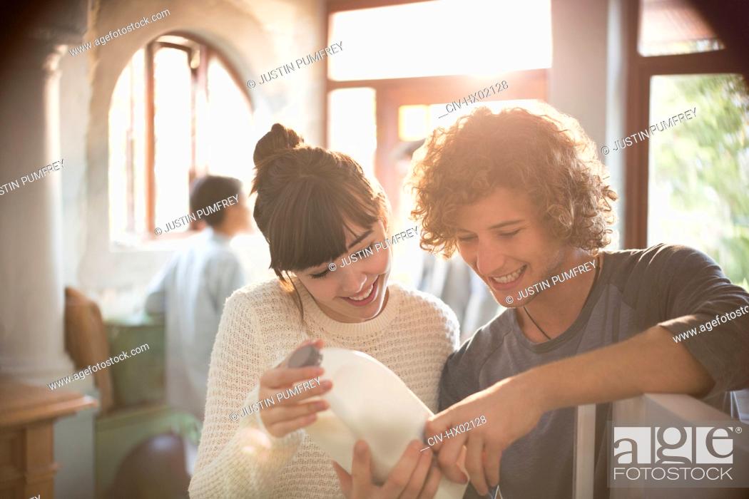 Stock Photo: Young couple roommates looking at expiration date on milk in kitchen.