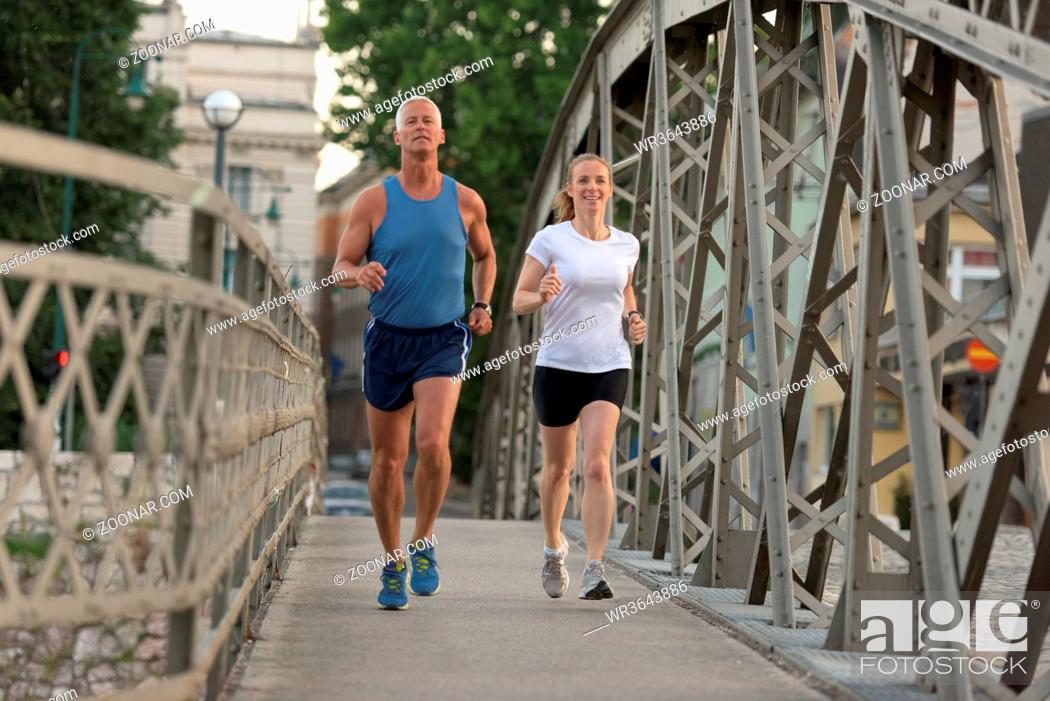 Stock Photo: healthy mature couple jogging in the city at early morning with sunrise in background.