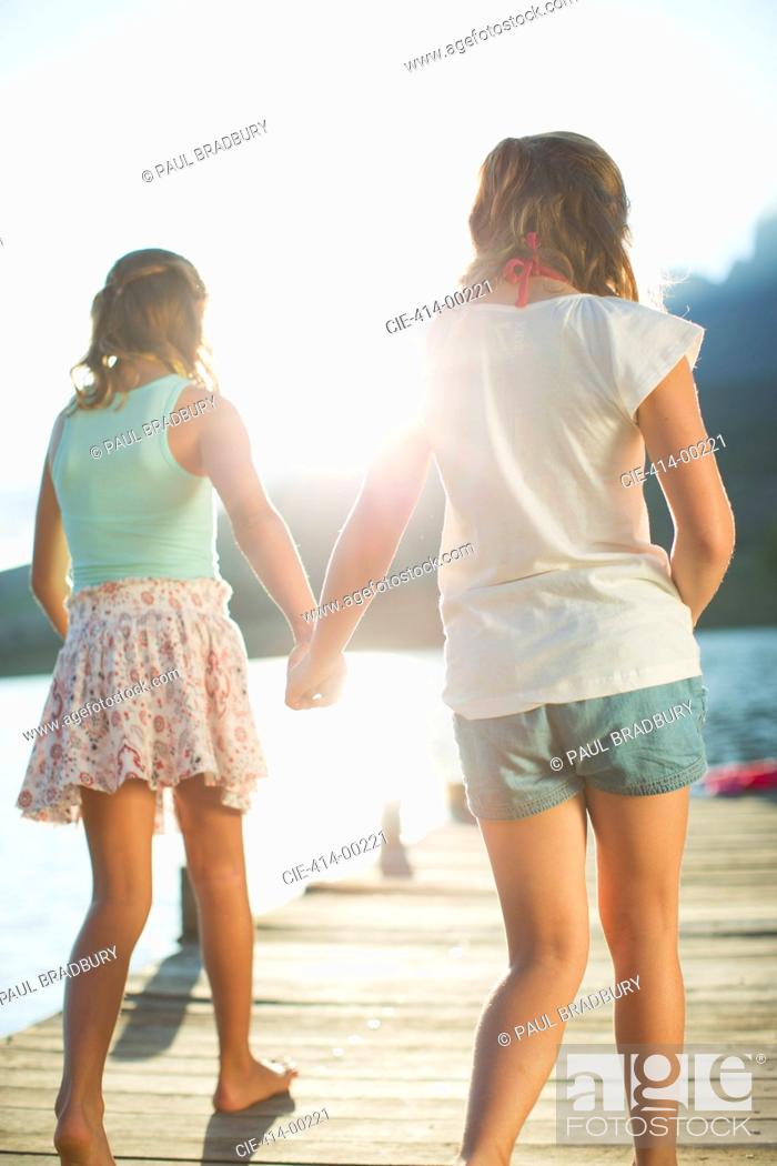 Stock Photo: Sisters holding hands on dock over lake.