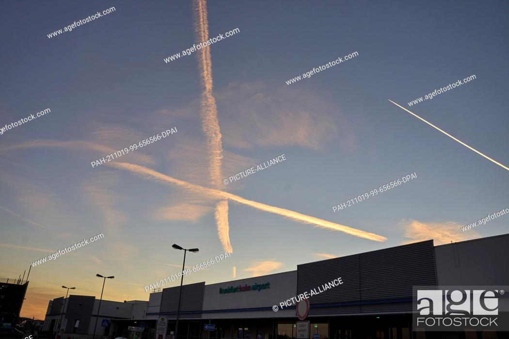 Stock Photo: 19 October 2021, Rhineland-Palatinate, Hahn: The vapour trails of two aircraft cross over the terminal of the former American military airport Hahn in Hunsrück.