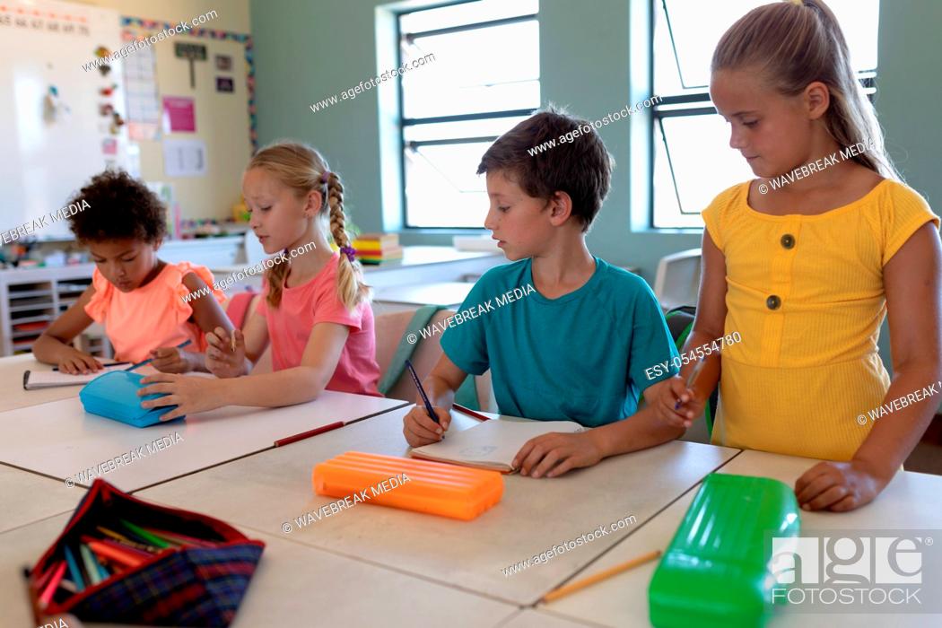 Stock Photo: Front view of a diverse group of four schoolchildren sitting at desks writing in an elementary school classroom, one Caucasian girl with blonde hair and wearing.