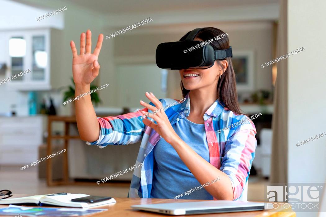 Stock Photo: Caucasian woman sitting by desk using a vr headset and smiling.