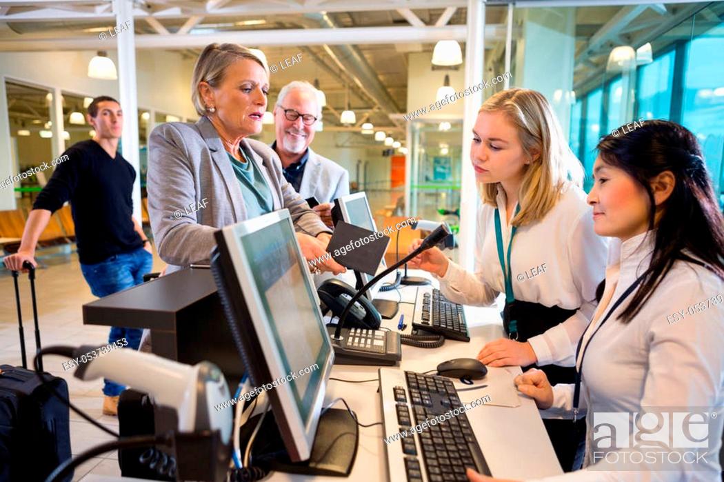 Stock Photo: Senior businesswoman holding passport while female staff working at airport check-in.