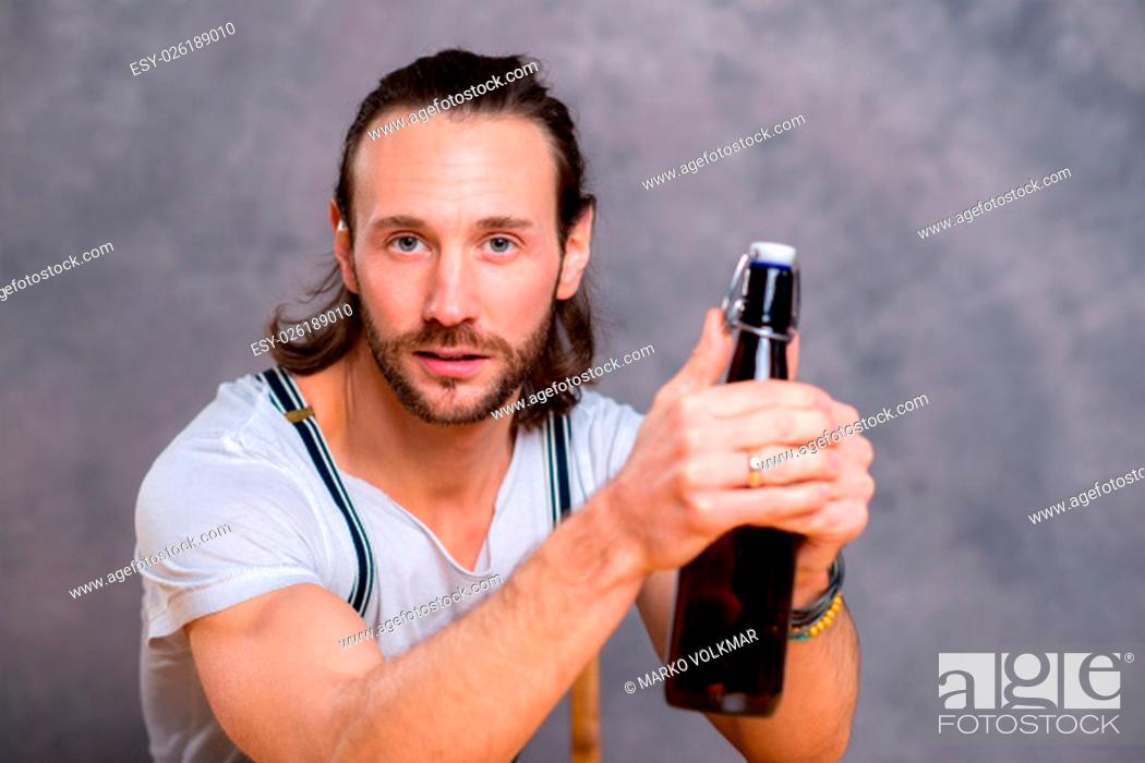 Stock Photo: young man in front of gray background opening a beer bottle.