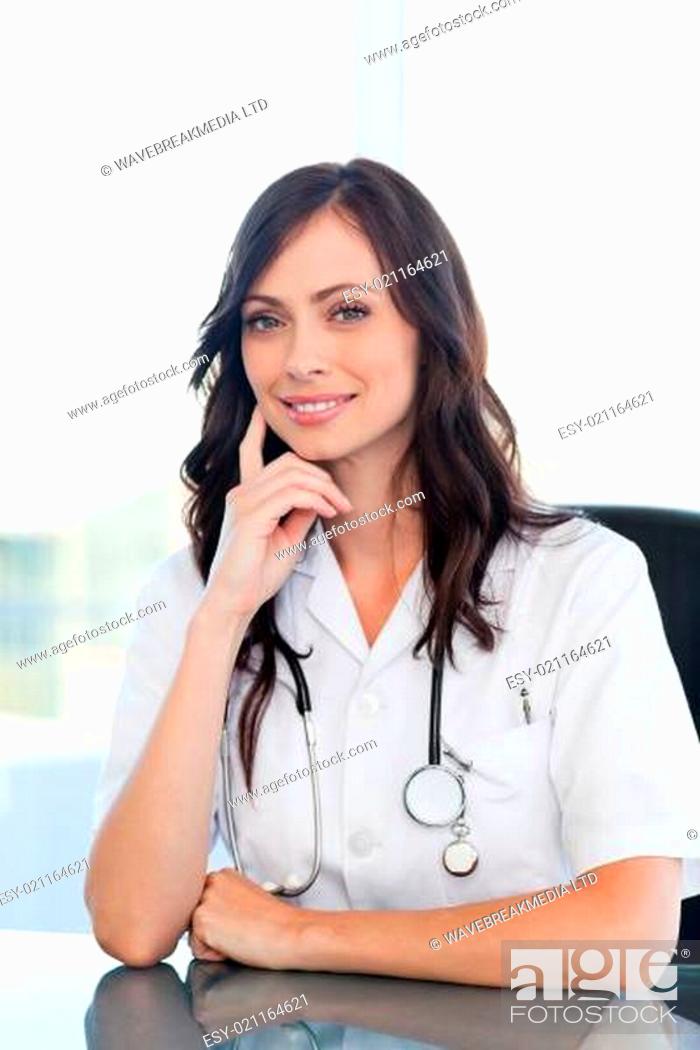 Stock Photo: Young doctor sitting at the desk wihile putting her finger against her cheek.