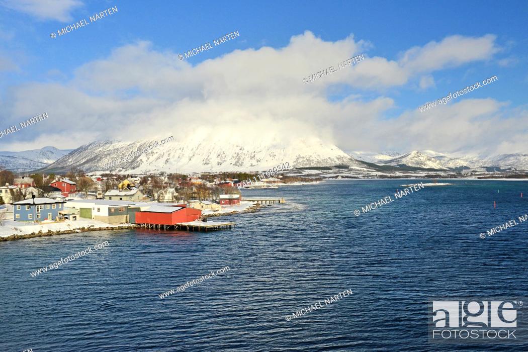 Stock Photo: Red boat house with boatbridge in the wavy water and other buildings from the small village Risøyhamn on the shore, 19 March 2017 | usage worldwide.