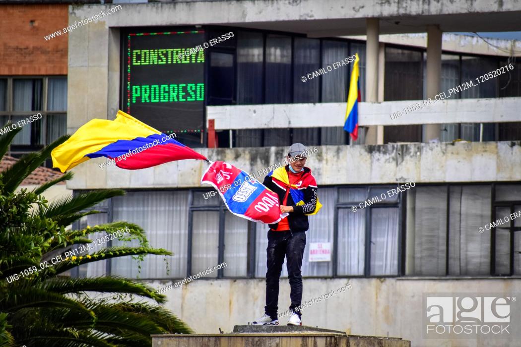 Stock Photo: Demostrator waves the flag of Colombia at the place where the statue of Antonio Narino was located, that was removed the night before with a fence behind him.