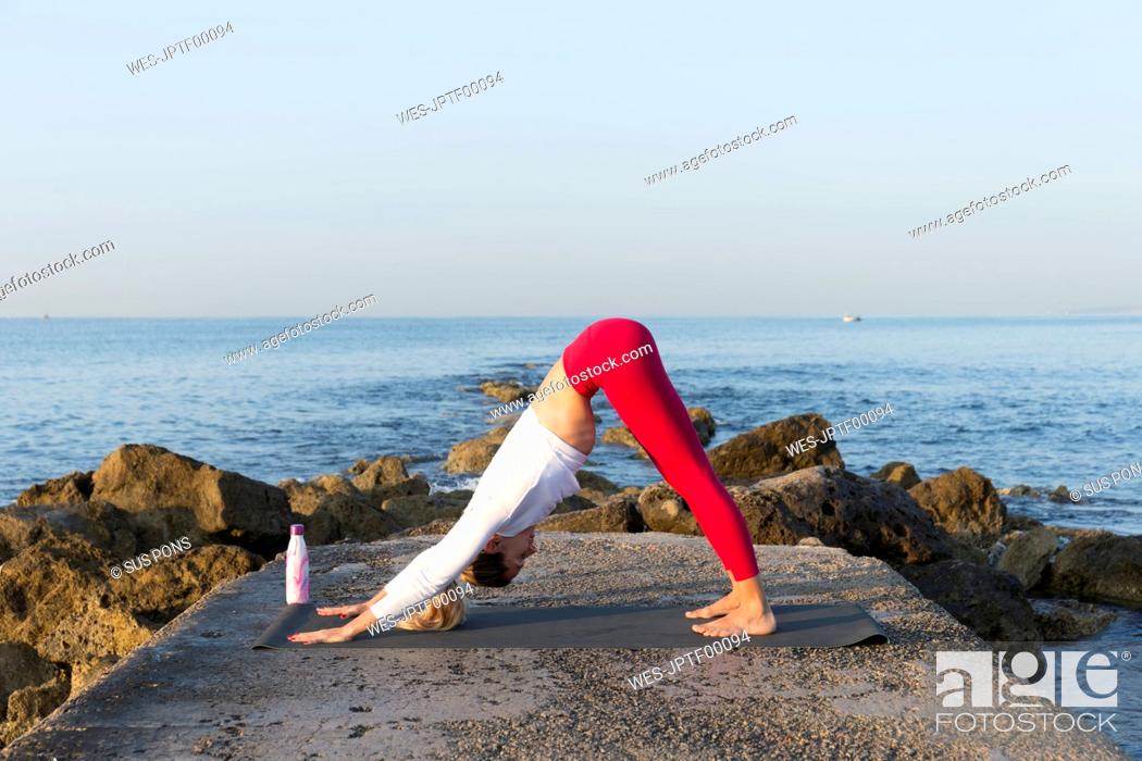 Stock Photo: Young woman practicing yoga on the beach, doing downward facing dog.