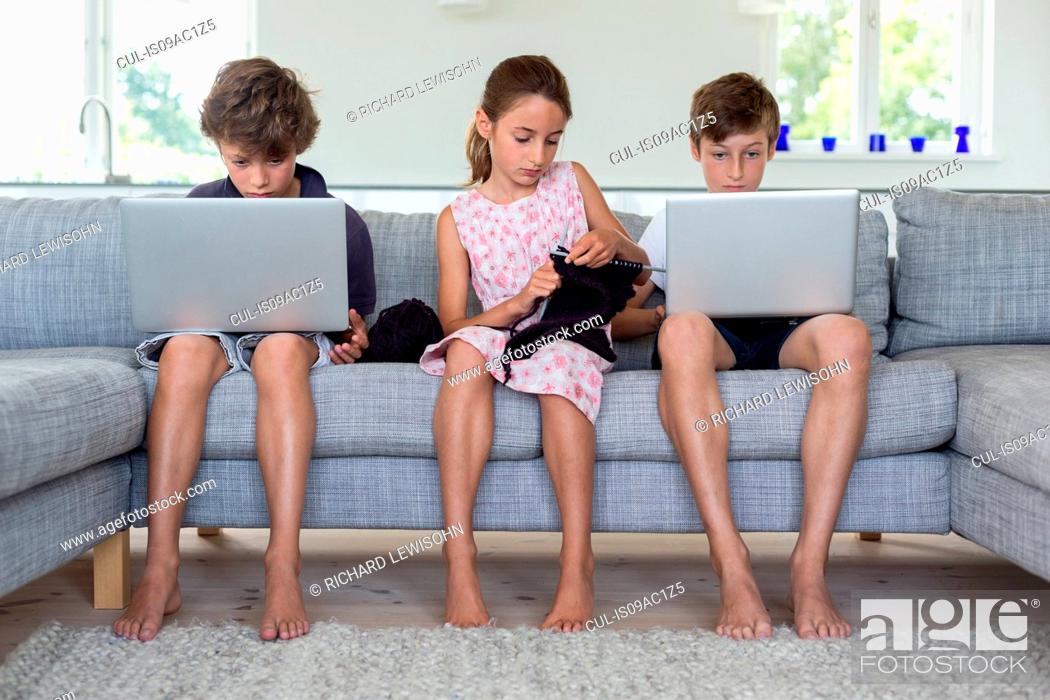 Stock Photo: Brothers and sister on sofa with computers and knitting.