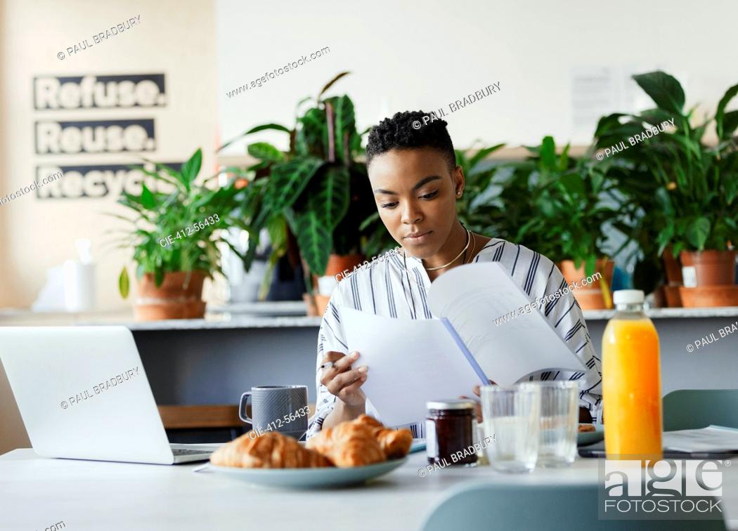 Stock Photo: Businesswoman reviewing paperwork at breakfast in office lounge.