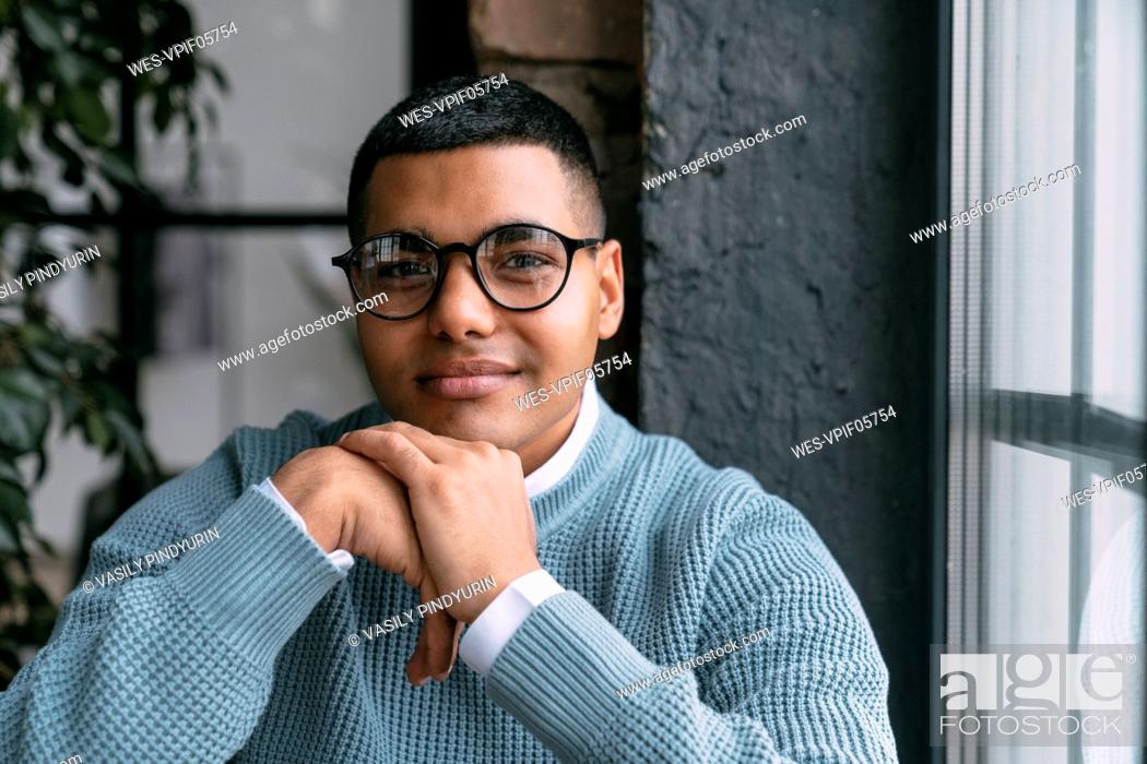 Stock Photo: Young man wearing eyeglasses by window at home.