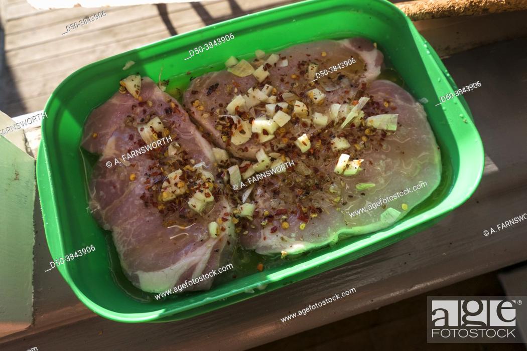 Photo de stock: Pork chops marinating in a green plastic container with chili flakes, garlic, lemon juice and oil.